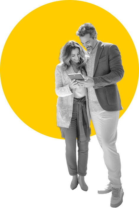 A man and woman smiling, looking at a phone on a yellow background.
