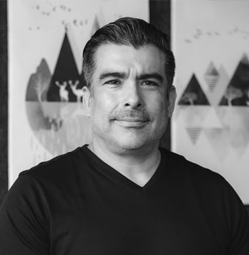 Shot1.jpg features a man smiling slightly, standing in front of abstract art posters.